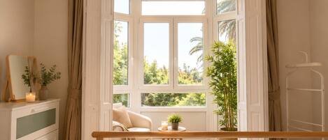 A bedroom with a large window, a bedside table, a chair, and a bed.
