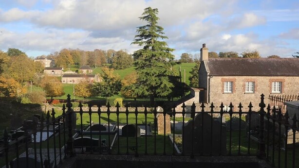 Un cimetière avec un grand arbre, un bâtiment en briques et une clôture.