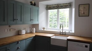 Une cuisine avec des meubles de couleur turquoise, un plan de travail en bois, une fenêtre donnant sur un beau paysage et un lave-vaisselle blanc.