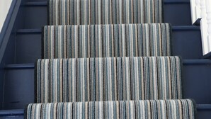 Un escalier dont les marches sont recouvertes d’une moquette à rayures et qui possède une rampe en bois.