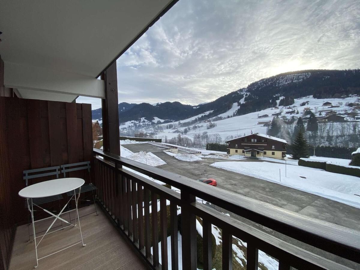 A balcony with a view of a snowy mountain landscape, a wooden railing, and a table.