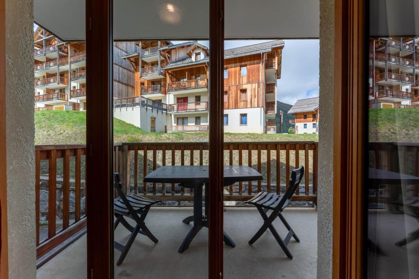 Un balcone con tavolo e sedie, affacciato su un edificio con numerosi balconi e una zona verde.