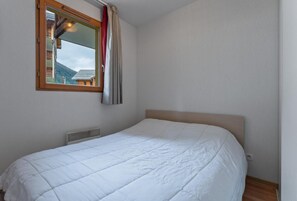 A bedroom with a bed, a window with curtains, a radiator, and a view of a building outside. - 200m from ski slopes, swimming pool, balcony, tv, ski locker, 30m², Les Orres (Les Orres)