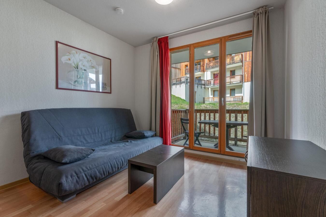 Ein modernes Wohnzimmer mit einer Couch, einem kleinen Tisch und Blick auf einen Balkon mit Geländer.