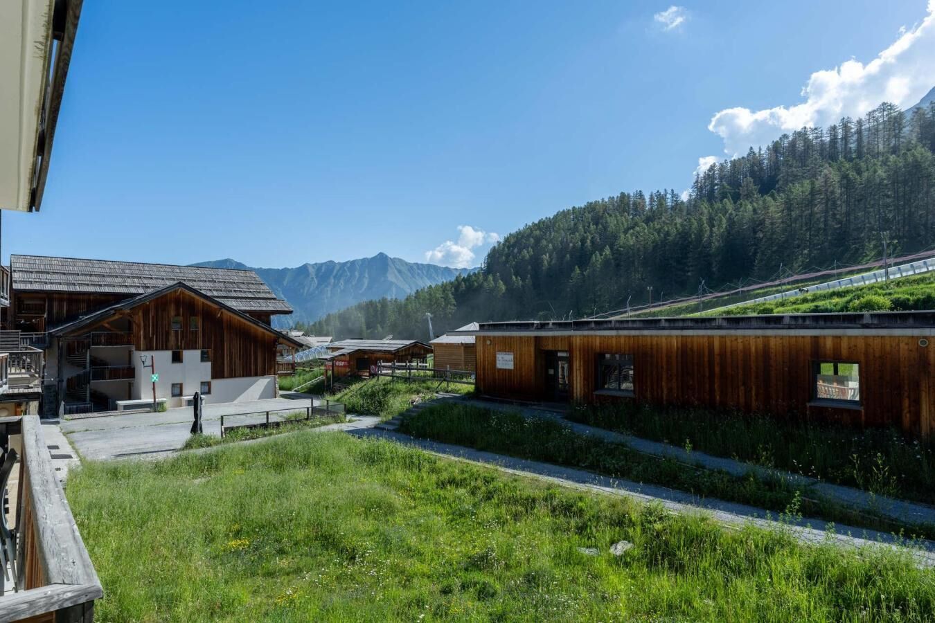A wooden building with a balcony, a grassy area, and a mountain backdrop.