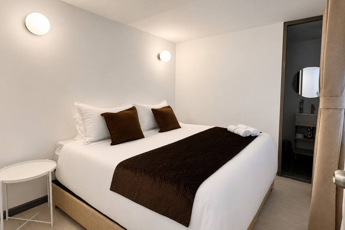 A hotel room with a bed, a round table, and a bathroom visible through an open door.