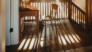 Una habitación de madera en el ático con techo inclinado, un escritorio con silla y vista al cielo a través del tejado.