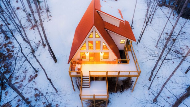 Una casa cubierta de nieve con un techo inclinado, un porche cubierto y una escalera que lleva a la entrada.