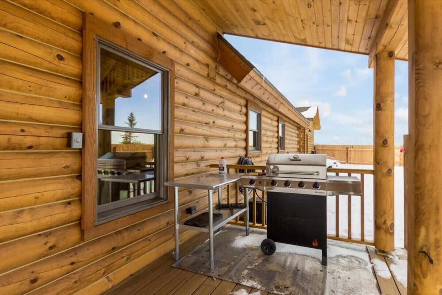 Eine Holzhütte mit einer Terrasse, einem Grill und einem Fenster mit Blick auf eine verschneite Landschaft.