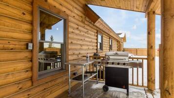 Eine Holzhütte mit einer Terrasse, einem Grill und einem Fenster mit Blick auf eine verschneite Landschaft.