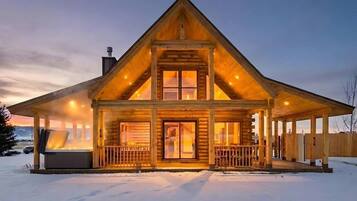 A log cabin with a large porch, a chimney, and a snow-covered ground.