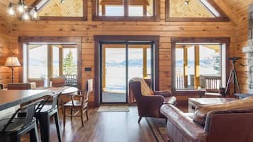 A log cabin interior with a dining area, a sofa, and a view of the mountains.