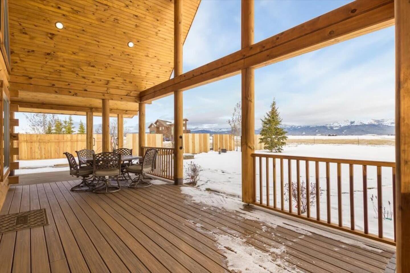 Eine überdachte Holzterrasse mit Tisch und Stühlen, mit Blick auf eine verschneite Landschaft und ferne Berge.