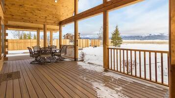 Eine überdachte Holzterrasse mit Tisch und Stühlen, mit Blick auf eine verschneite Landschaft und ferne Berge.