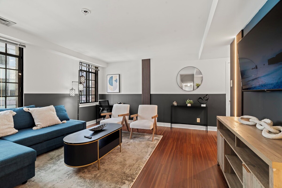 Ein modernes Wohnzimmer mit einem blauen Sofa, zwei weißen Sesseln, einem schwarzen Couchtisch und einer Holz-TV-Konsole.
