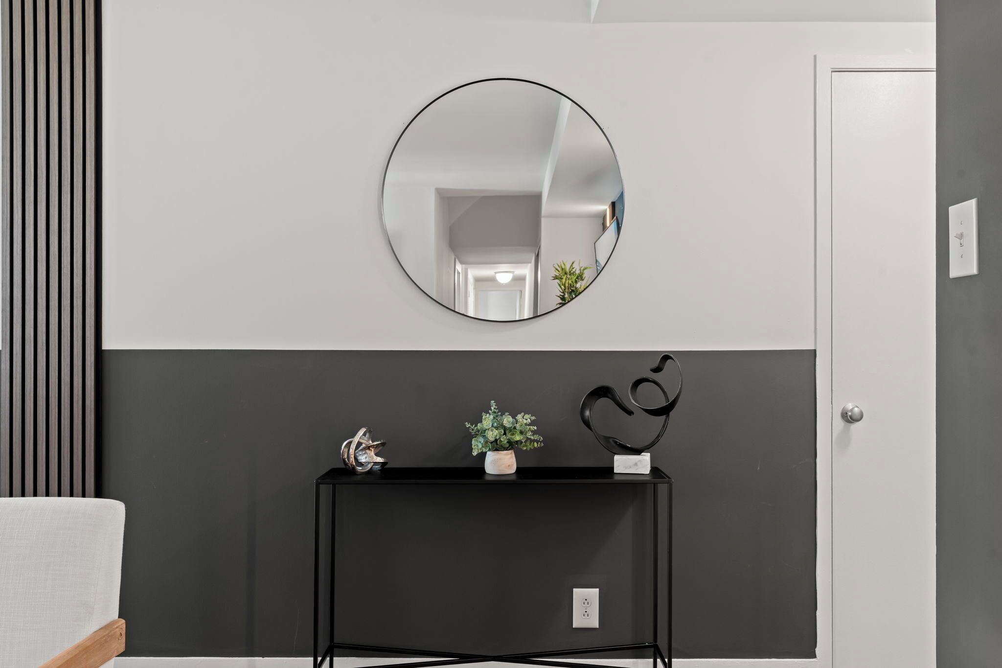 Un couloir moderne avec une console noire, un miroir rond et une plante en pot.
