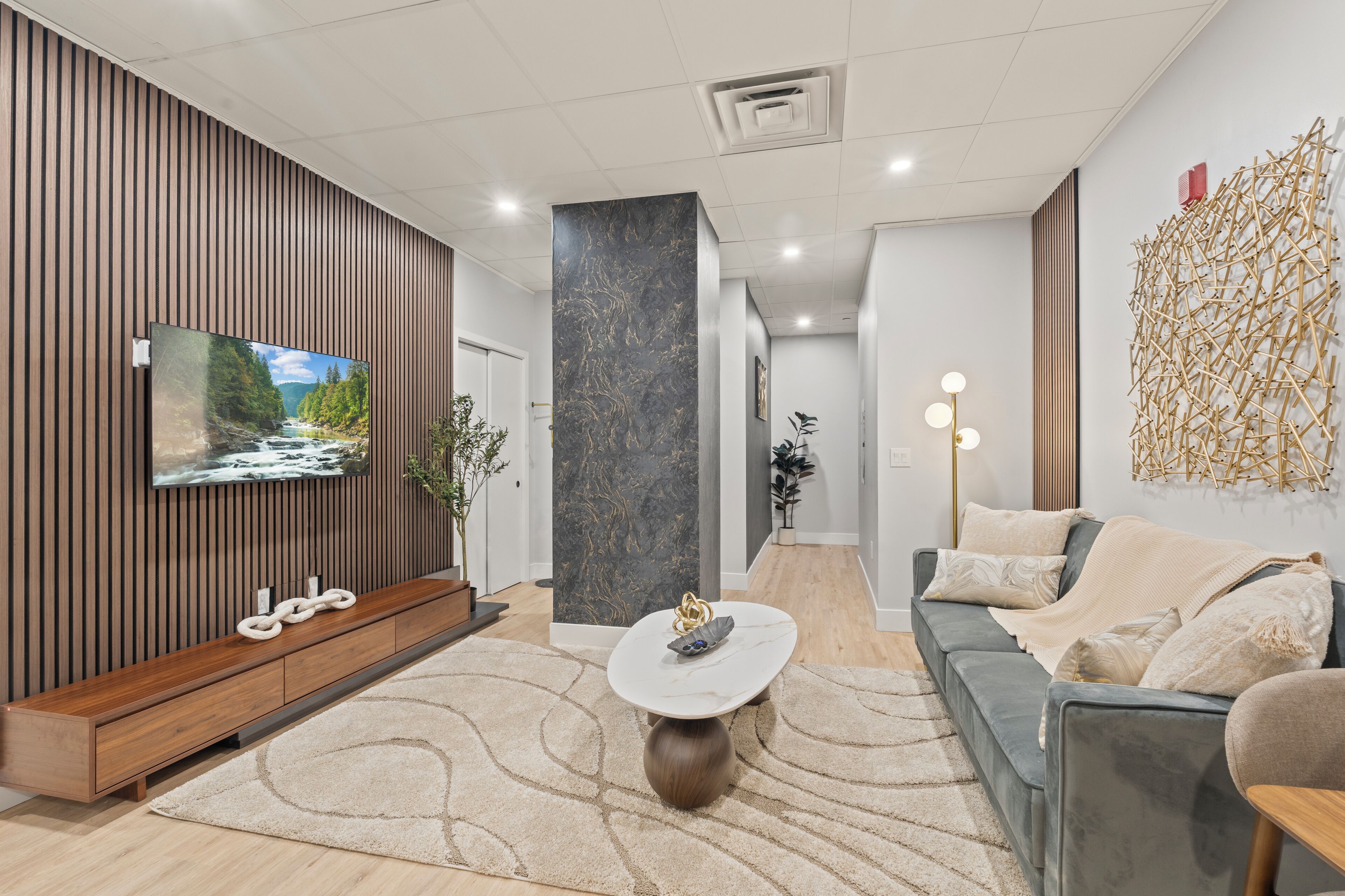 A modern living room with a flat-screen TV, a wooden entertainment unit, a grey sofa, and a coffee table.