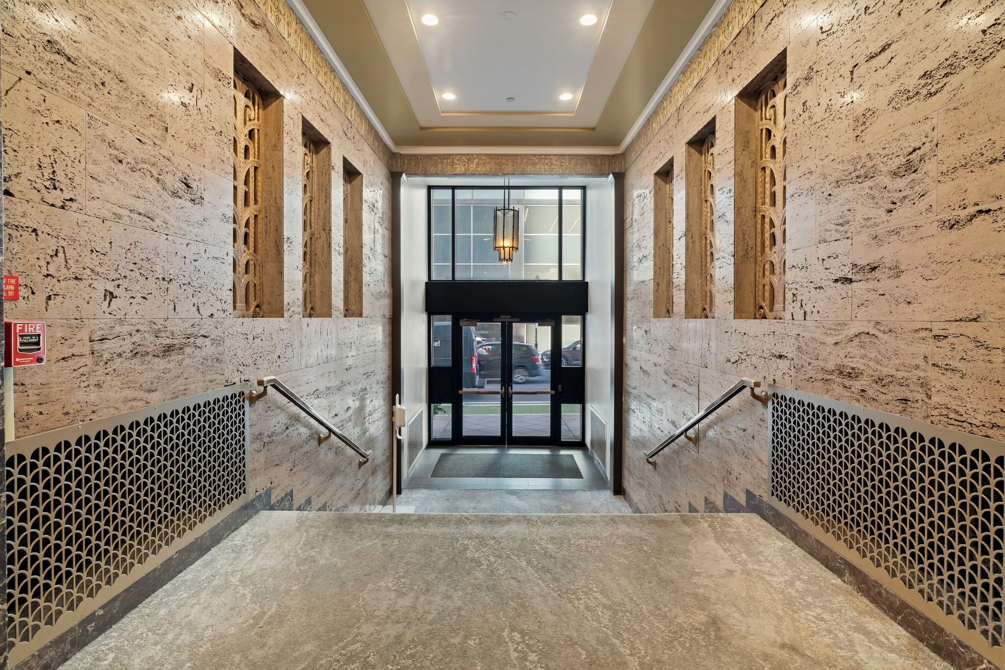 A marble staircase leading to a glass door entrance with a fire alarm sign on the wall.