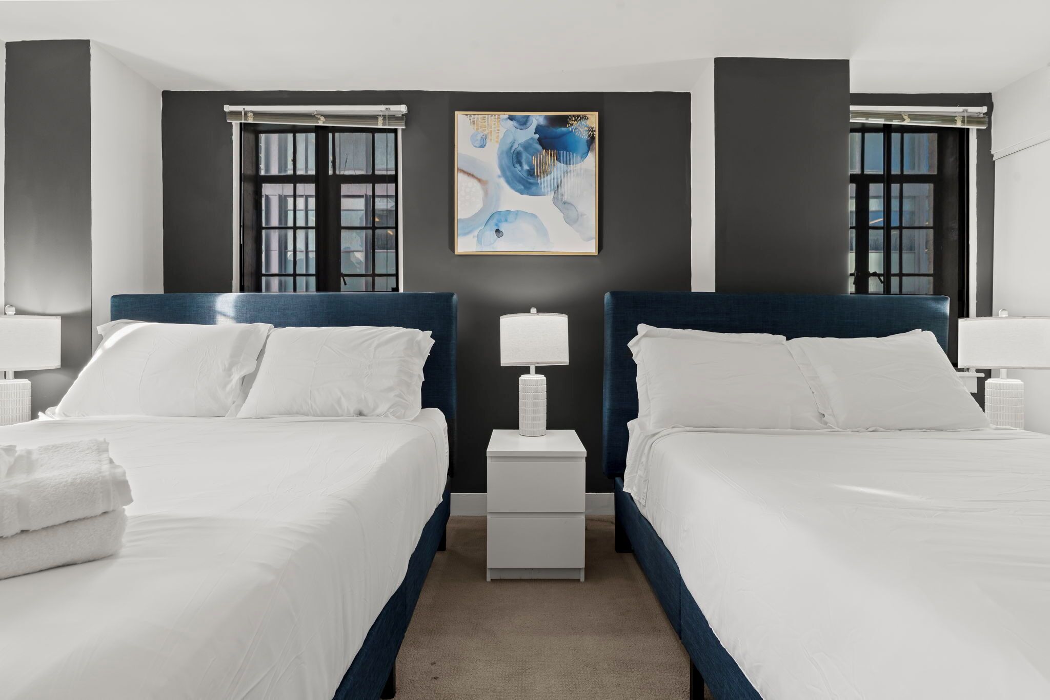 Une chambre d’hôtel avec deux lits, une table de chevet, une lampe et un tableau au mur.