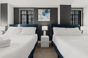 A hotel room with two beds, a nightstand, a lamp, and a painting on the wall.
