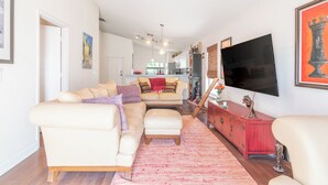 A living room with a sofa, ottoman, and a TV mounted on the wall. - THE CLAR by EVRH (Orlando)