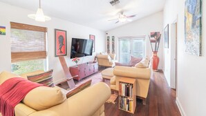 A living room with a sofa, a coffee table, a TV, and artwork on the walls. - THE CLAR by EVRH (Orlando)