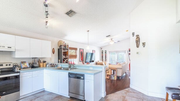 A modern kitchen with white cabinets, a dishwasher, and a central island. - THE CLAR by EVRH (Orlando)