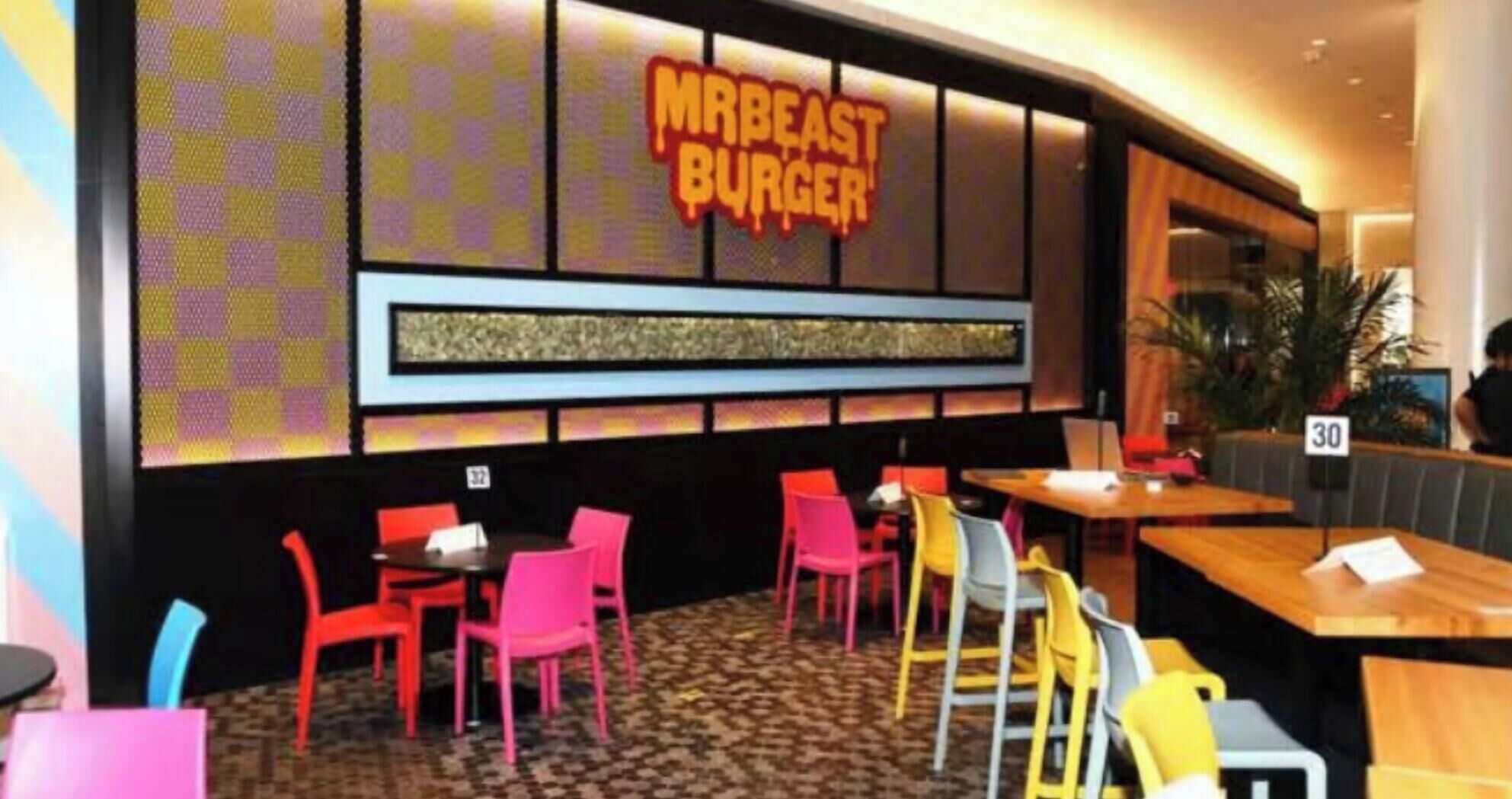 L’intérieur d’un restaurant présente un mur orné d’un motif à carreaux, un panneau néon indiquant « MRBEAST BURGER », ainsi que de nombreuses tables et chaises.