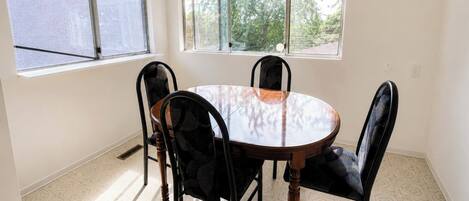 A dining area with a round table and four chairs, large windows, and a patterned floor.