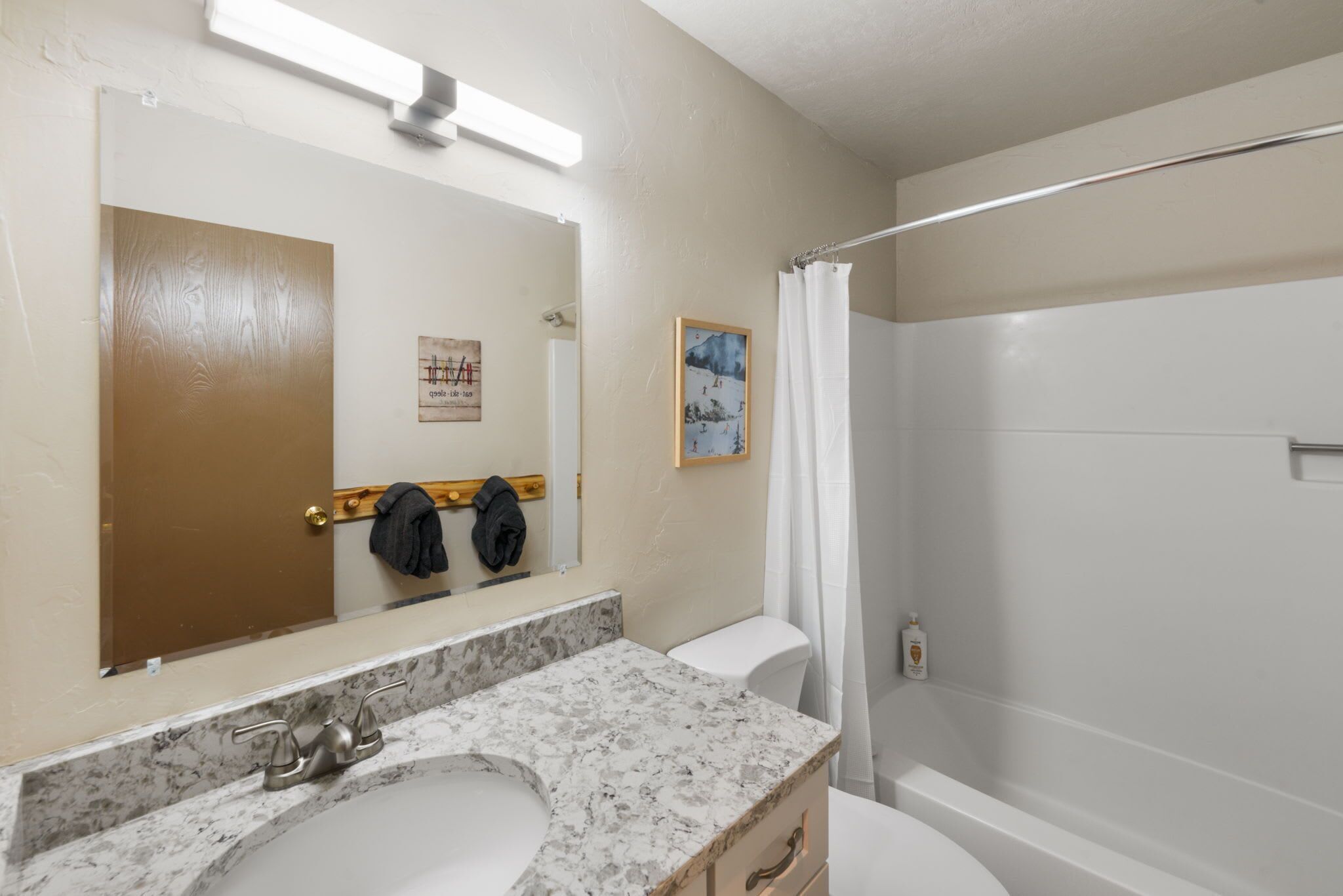 Une salle de bain avec un lavabo en marbre, des toilettes, une douche avec un rideau et un miroir muni d’un porte-serviettes.
