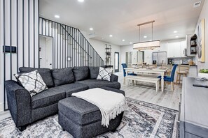 Ein modernes Wohnzimmer mit einem grauen Ecksofa, einer weißen Decke und einem gemusterten Teppich.