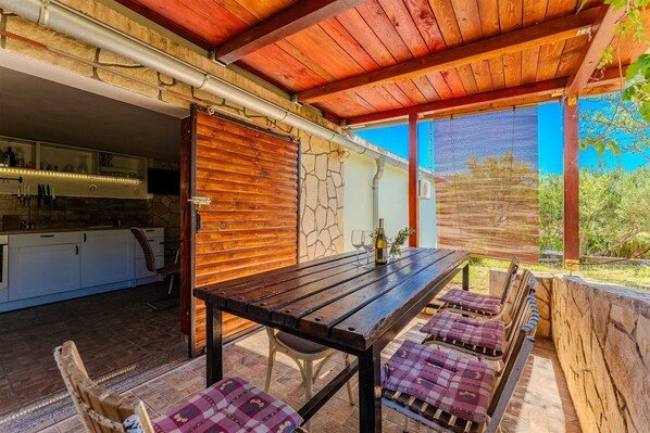 Un espacio exterior para comer con mesa y sillas de madera, pared de piedra y vista al cielo.