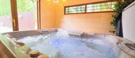 Un bain à remous avec jets d’eau, des murs en bois, une fenêtre et une plante.
