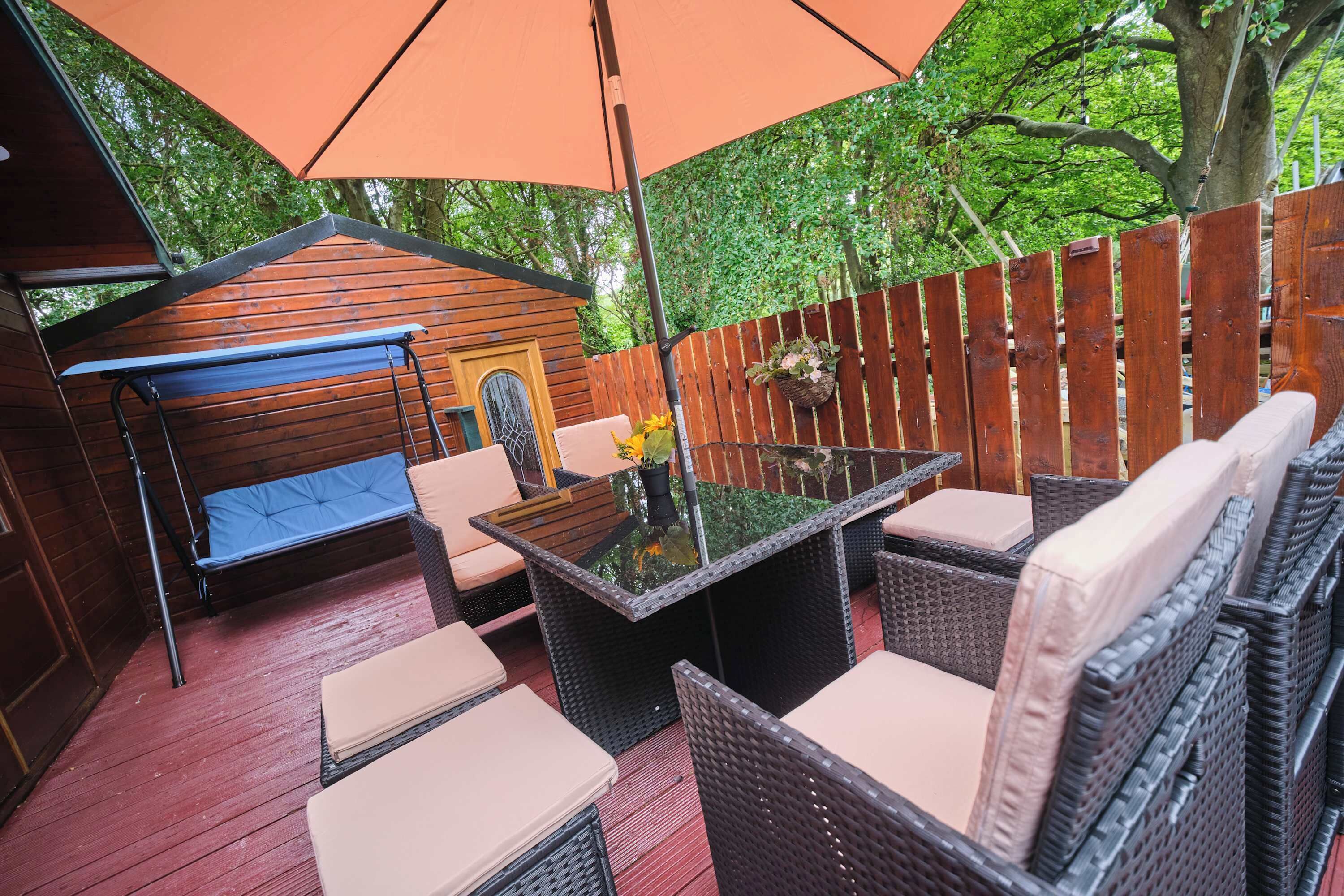 An outdoor patio with wicker furniture, a glass-top table, and a swing seat.