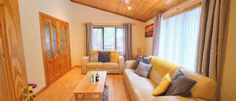 A living room with a wooden ceiling, a sofa set, a coffee table, and a window with curtains.