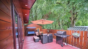 A wooden deck with outdoor furniture, a grill, and a wooden fence.