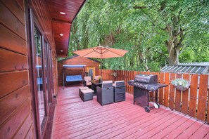 Una terraza de madera con mobiliario exterior, una parrilla y una valla de madera.
