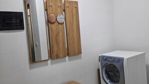 Une buanderie équipée d’un lave-linge, d’un meuble en bois et d’un miroir avec des crochets.