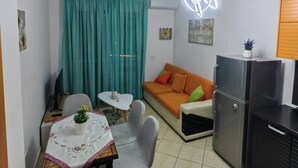 Un espace de vie compact comprenant un coin repas, un canapé, un réfrigérateur et un luminaire fixé au plafond.