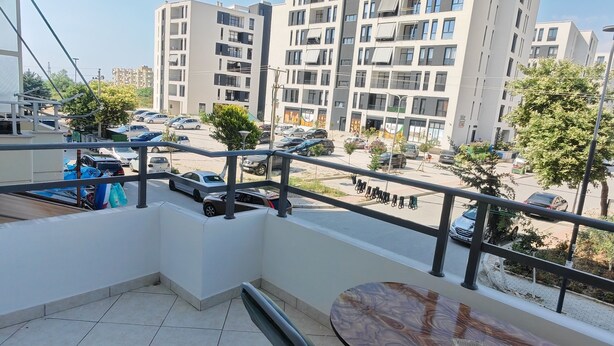 Un balcon avec une table et des chaises, une vue sur un parking et, au loin, des immeubles d’appartements modernes.