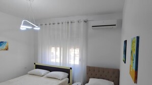 Une chambre avec deux lits, une petite table, un appareil de climatisation et un luminaire au plafond.