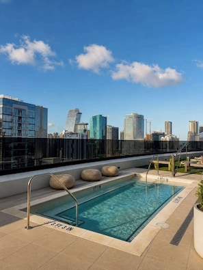Una piscina en la azotea con un horizonte urbano de fondo, rodeada de edificios modernos.