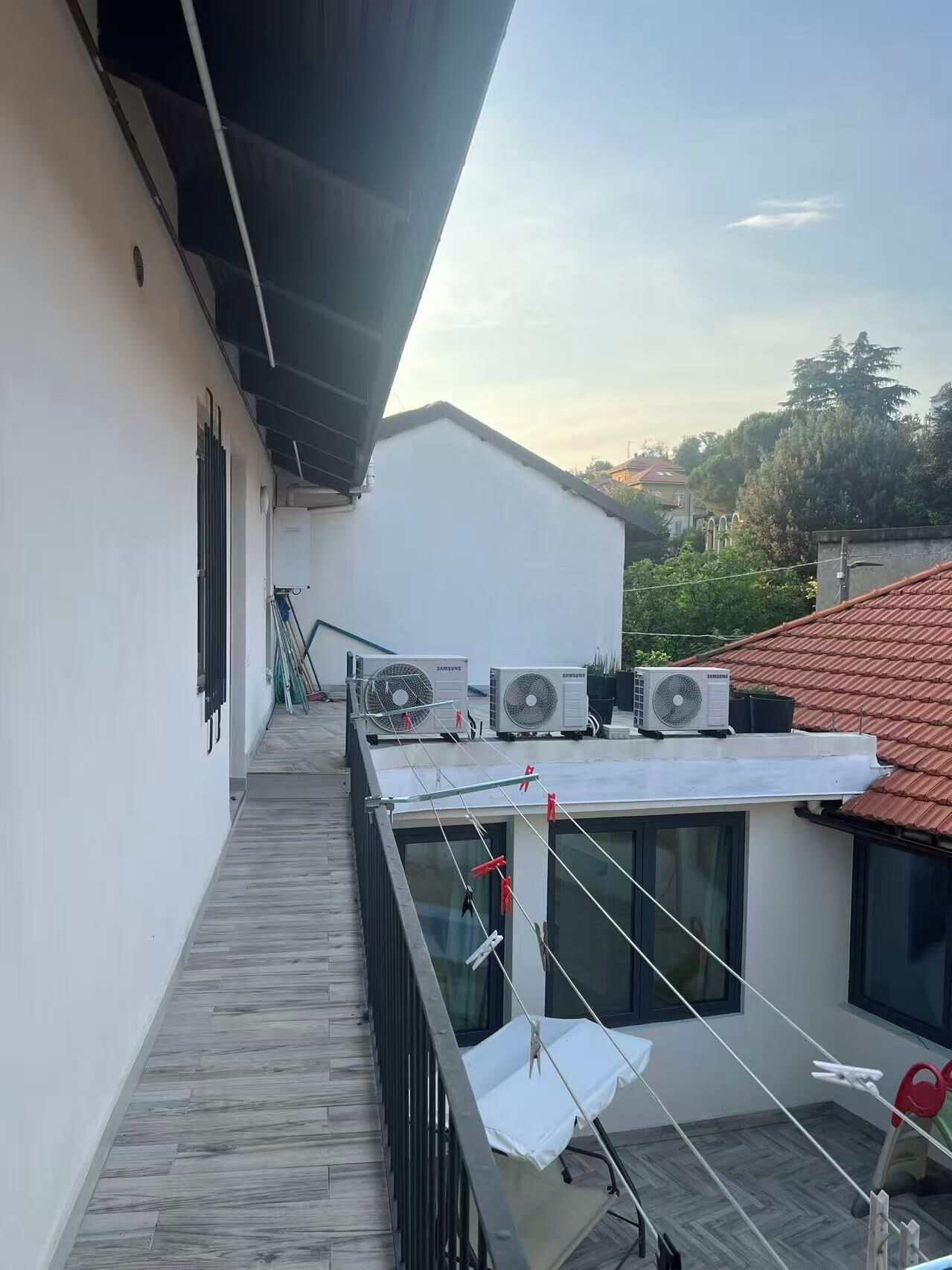 Eine Dachterrasse mit Klimaanlagen, einem Holzboden und Blick auf umliegende Gebäude.
