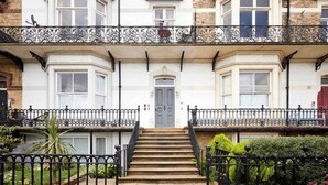 A two-story building with a central entrance, a staircase, and a balcony with ornate iron railings. - Host Stay Kingsley House (Saltburn-by-the-Sea)
