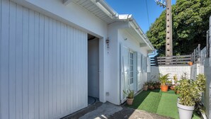 Un bâtiment blanc avec une porte de garage, un petit jardin agrémenté de plantes en pot et un chemin en béton.