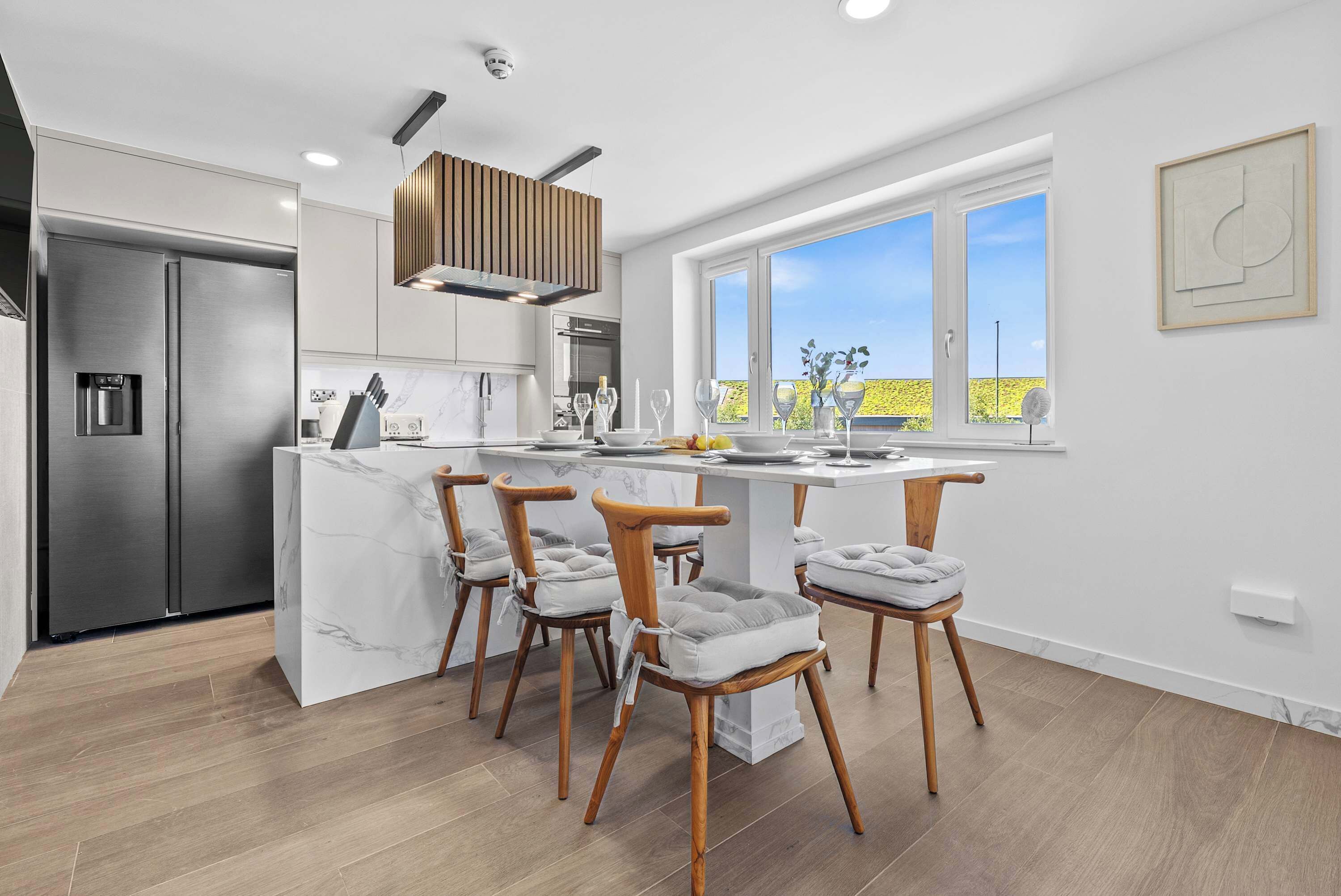 A modern kitchen with a marble island, stainless steel appliances, and wooden chairs.