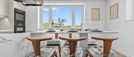 Une cuisine moderne avec un îlot central, des chaises en bois et une vue sur l’extérieur.