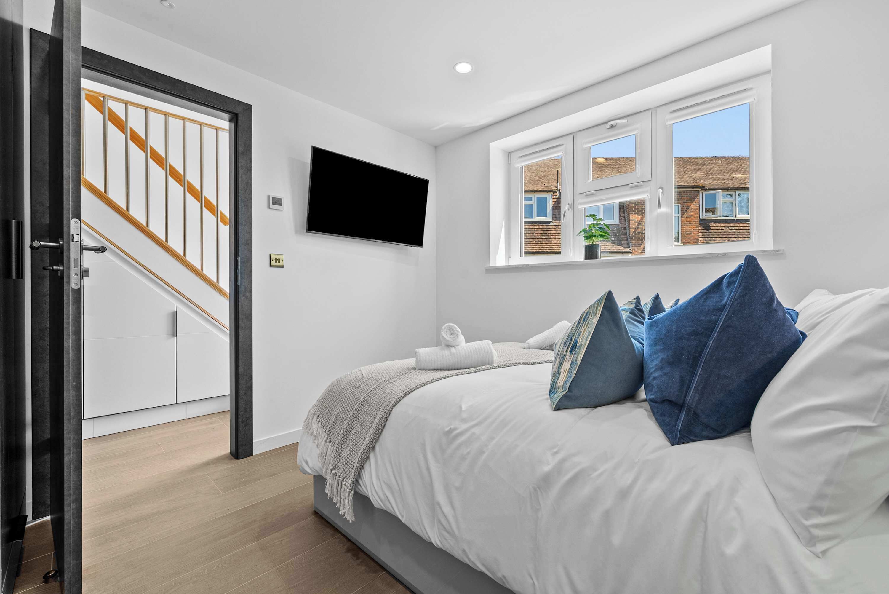 A bedroom with a bed, a TV, a window, a staircase, and a door.
