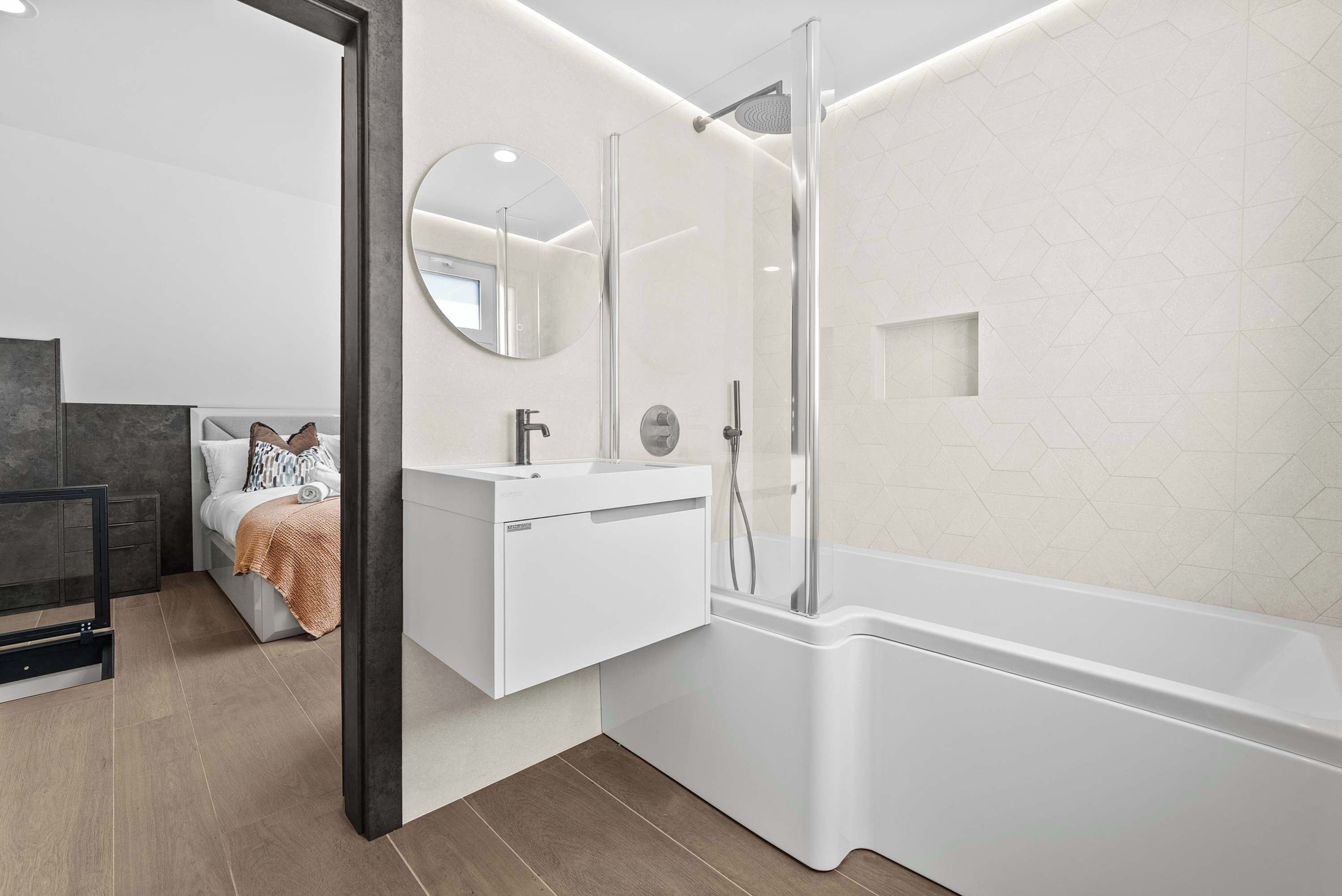 A modern bathroom with a glass-enclosed shower, a white vanity, and a bed with a view.