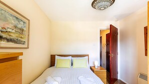 Una habitación de hotel con una cama, un aparador de madera, un cuadro en la pared y una puerta que da a otra habitación.